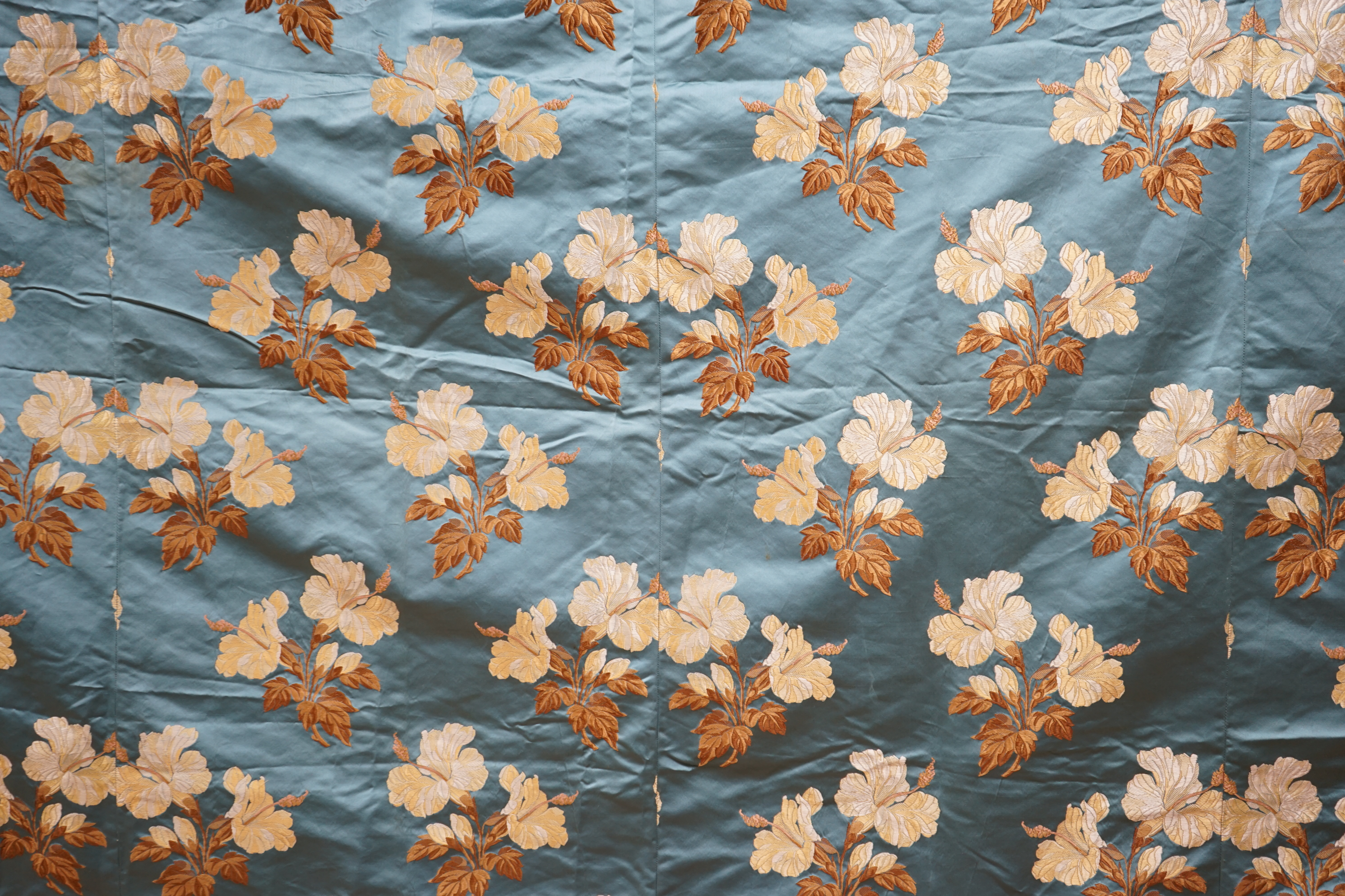 A turquoise satin floral silk brocaded panel of four 59cm widths, boldly embroidered in yellow and brown strays of lilies, the panel possibly part of a pelmet or half tester bed, each spray being 21cm high as a diagonal